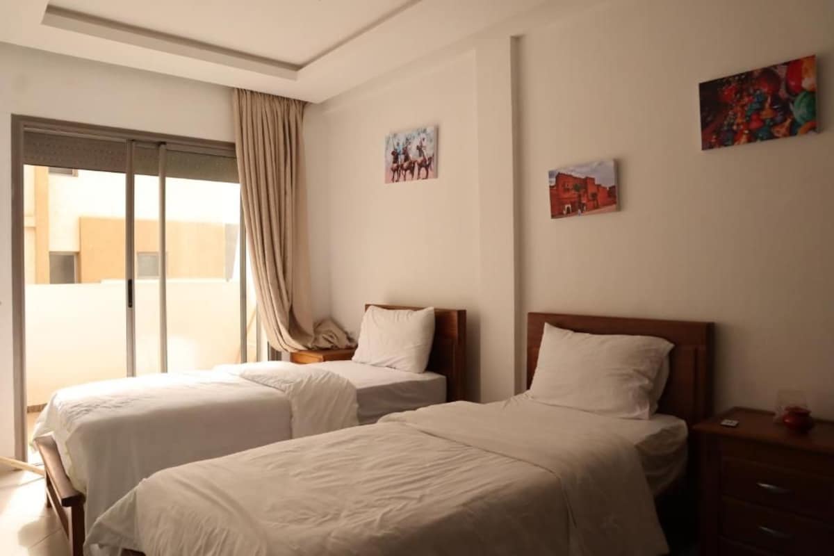 Ein Hotelzimmer mit zwei Betten, einer Schiebetür zu einem Balkon und Bildern an den Wänden.