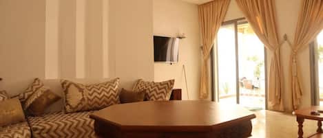 A room with a sofa set, a wooden table, and a television mounted on the wall.