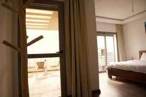 Habitación de hotel con cama, balcón con sillas y vista al exterior.