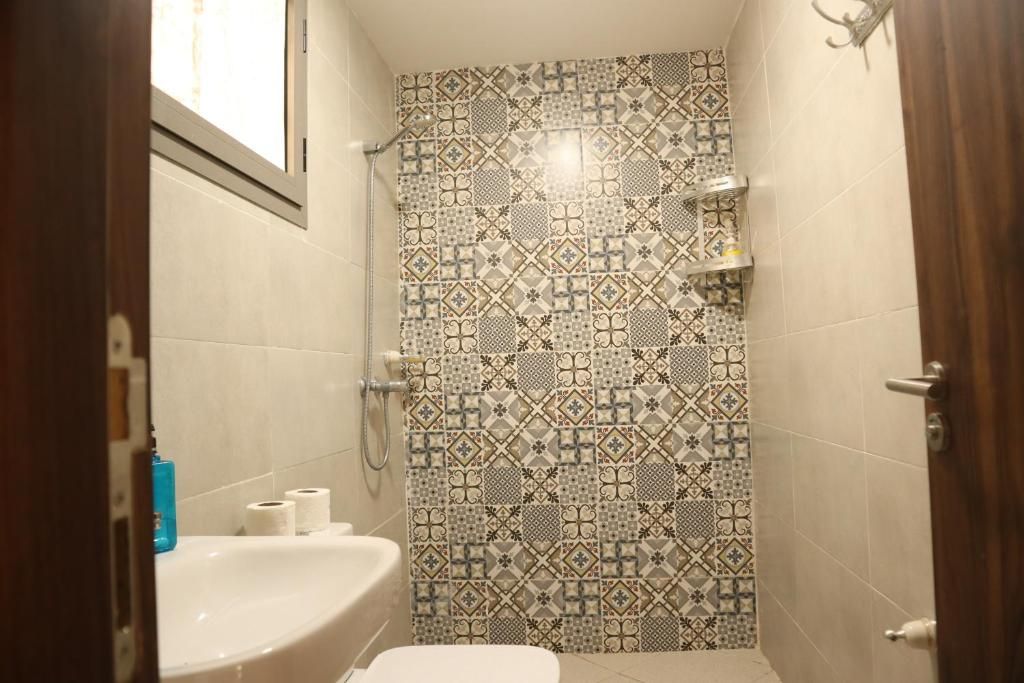 A bathroom with a patterned tile wall, a white sink, and a shower.