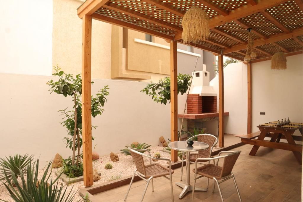 A patio with a round table and chairs, a wooden pergola, and a brick oven.