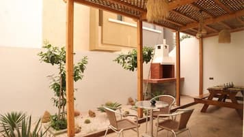 Un patio con una mesa redonda y sillas, una pérgola de madera y un horno de ladrillo.
