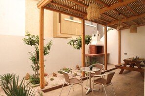 A patio with a round table and chairs, a wooden pergola, and a brick oven. - Surf and Stay Villa Anza (Agadir)