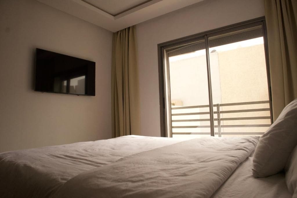 Habitació d'hotel amb un llit, una televisió penjada a la paret i una finestra amb cortines.