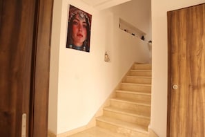 Una escalera con barandilla de madera, un cuadro colgado en la pared y un estante con objetos.
