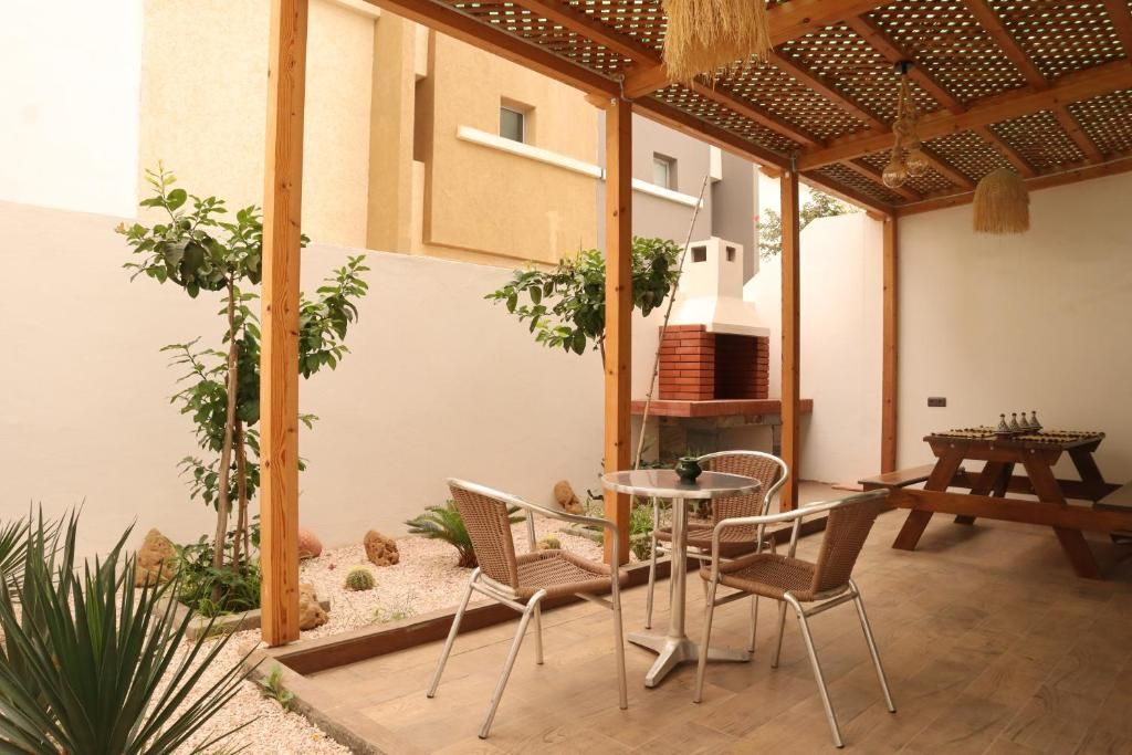 An outdoor patio with a round table and chairs, a brick oven, and a wooden pergola.