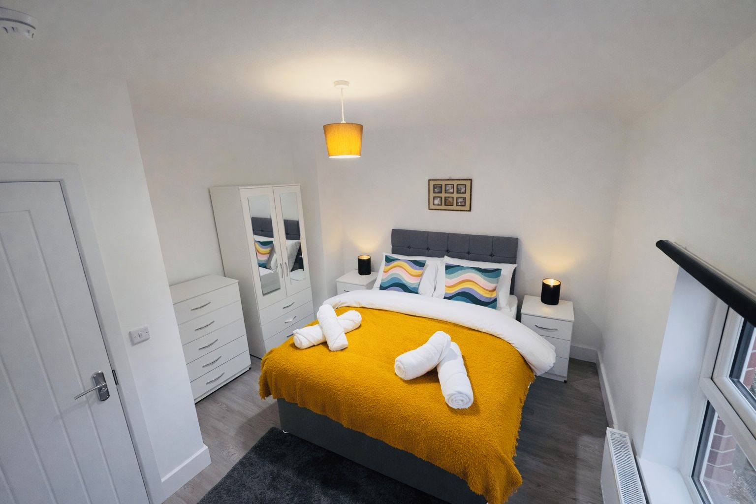 A bedroom with a bed, bedside tables, a wardrobe, a mirror, and a hanging light fixture.