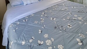 Un dormitorio con cama, mesita de noche, lámpara, ventana con cortinas y un cuadro en la pared.