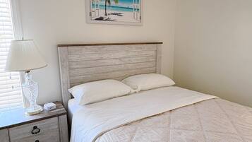 A bedroom with a bed, a nightstand, a lamp, and a painting of a beach scene.