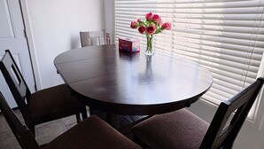 Un comedor con una mesa redonda, cuatro sillas, un jarrón con flores y una ventana con persianas.