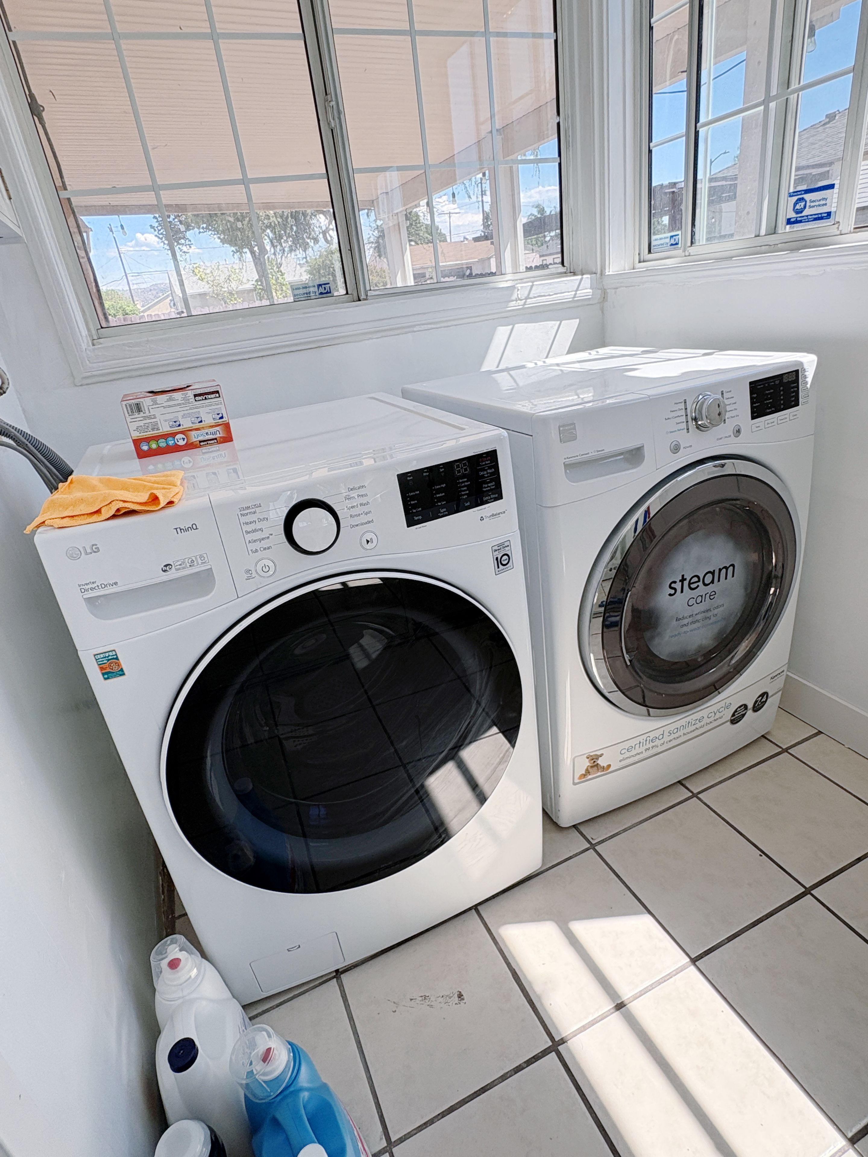 Un espace buanderie comprenant deux machines à laver, une bouteille de lessive et un chiffon de nettoyage.