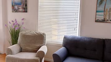 A living room with a beige armchair, a dark grey sofa, a wooden coffee table with a vase of yellow flowers, and a painting of a beach scene.