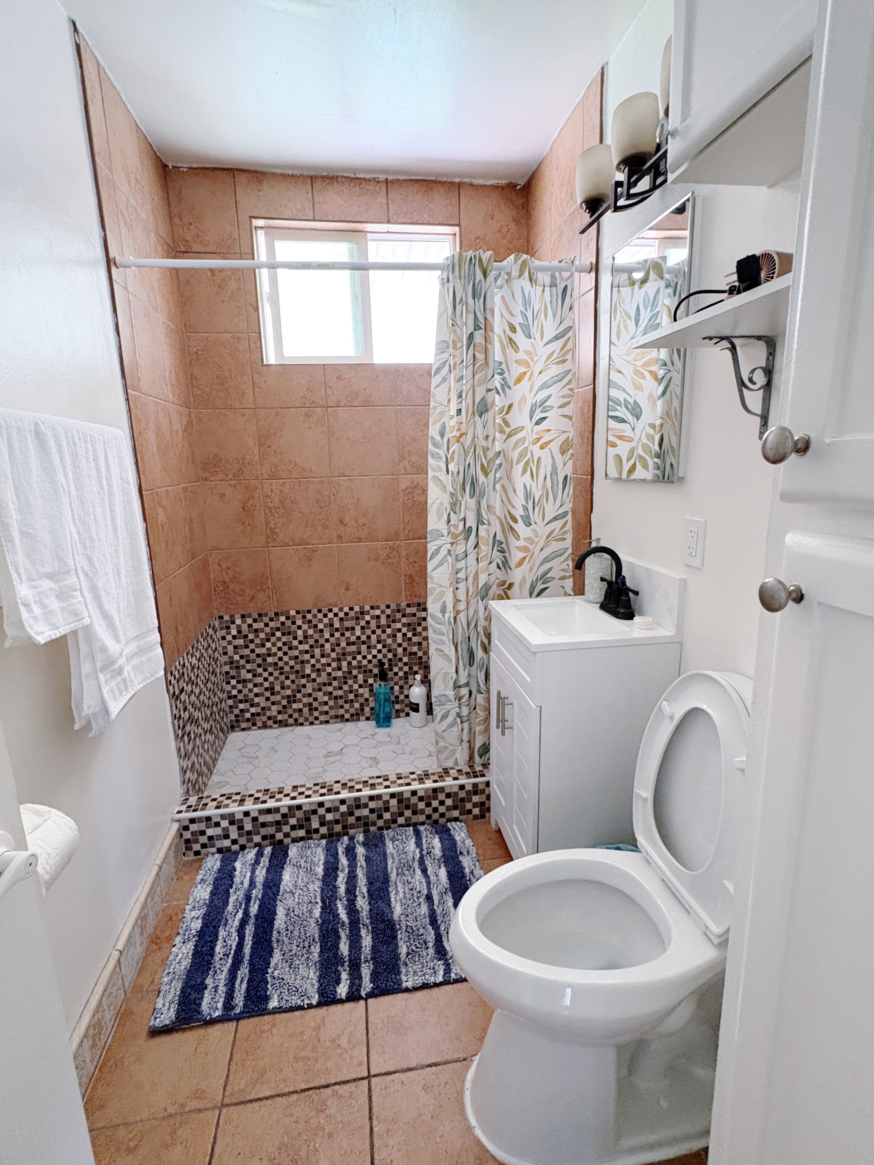 Ein Badezimmer mit Dusche, Toilette, Waschbecken und einem Fenster.
