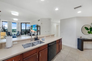 A modern kitchen with a dishwasher, double sink, and a dining area with a view.