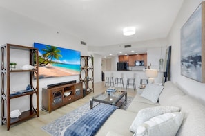 Ein modernes Wohnzimmer mit Fernseher, einer Couch, einem Couchtisch und einer Küche im Hintergrund.