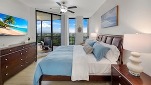 Ein Schlafzimmer mit Bett, Schminktisch, Deckenventilator, Fernseher und Blick ins Freie.