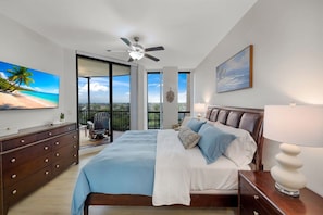 Quarto com cama, cômoda, ventoinha no teto, televisão e vista para o exterior.