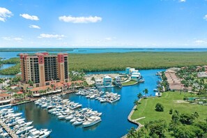 Ein Yachthafen mit mehreren vertäuten Booten, ein großes Hotelgebäude und freie Sicht auf das umliegende Wasser und die grüne Landschaft.