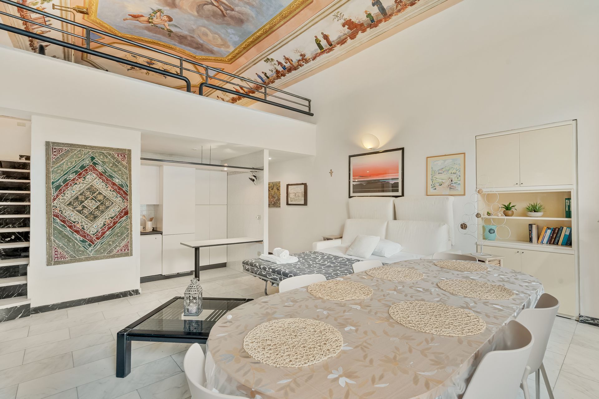 Un'ampia camera d'albergo con un letto grande, un angolo salotto, un tavolo da pranzo, una scala e vista sul cielo.