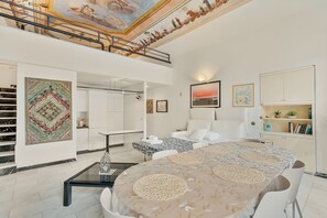 Un'ampia camera d'albergo con un letto grande, un angolo salotto, un tavolo da pranzo, una scala e vista sul cielo.