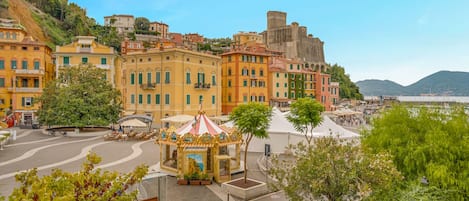 A coastal town with historic buildings, a central square with a carousel, and a view of the sea.