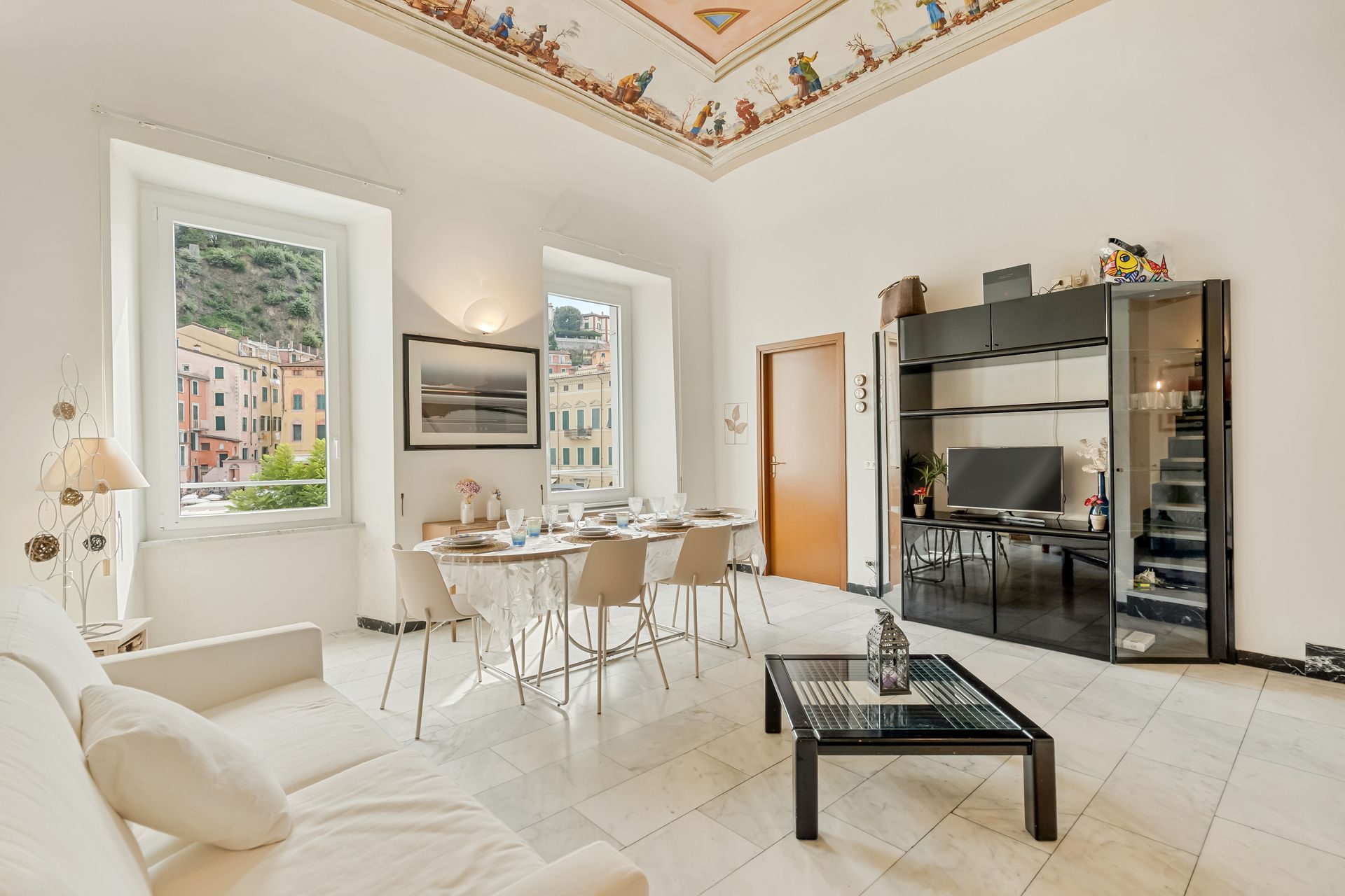Un soggiorno moderno con zona pranzo, un divano, un tavolino e una TV su un mobile nero.