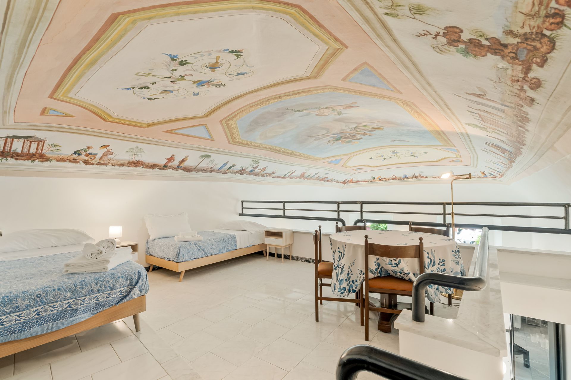 Habitación de hotel con cama, escritorio y silla. El techo presenta un diseño floral.
