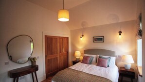 Un dormitorio con cama, lámparas de noche, un espejo, una puerta de madera y un cuadro en la pared.