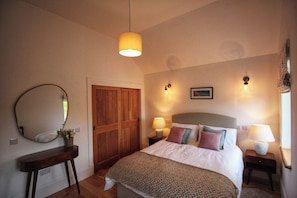 Un dormitorio con cama, lámparas de noche, un espejo, una puerta de madera y un cuadro en la pared.