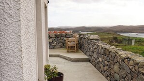 Un balcón con un muro de piedra, una silla de madera y una planta en maceta.
