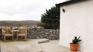 Un patio con dos sillas de madera, una mesa, un muro de piedra y una planta en maceta.