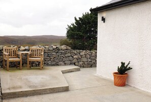 Un patio con dos sillas de madera, una mesa, un muro de piedra y una planta en maceta.