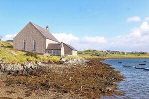 Una casa costera de exterior de piedra, techo inclinado y vista al mar.