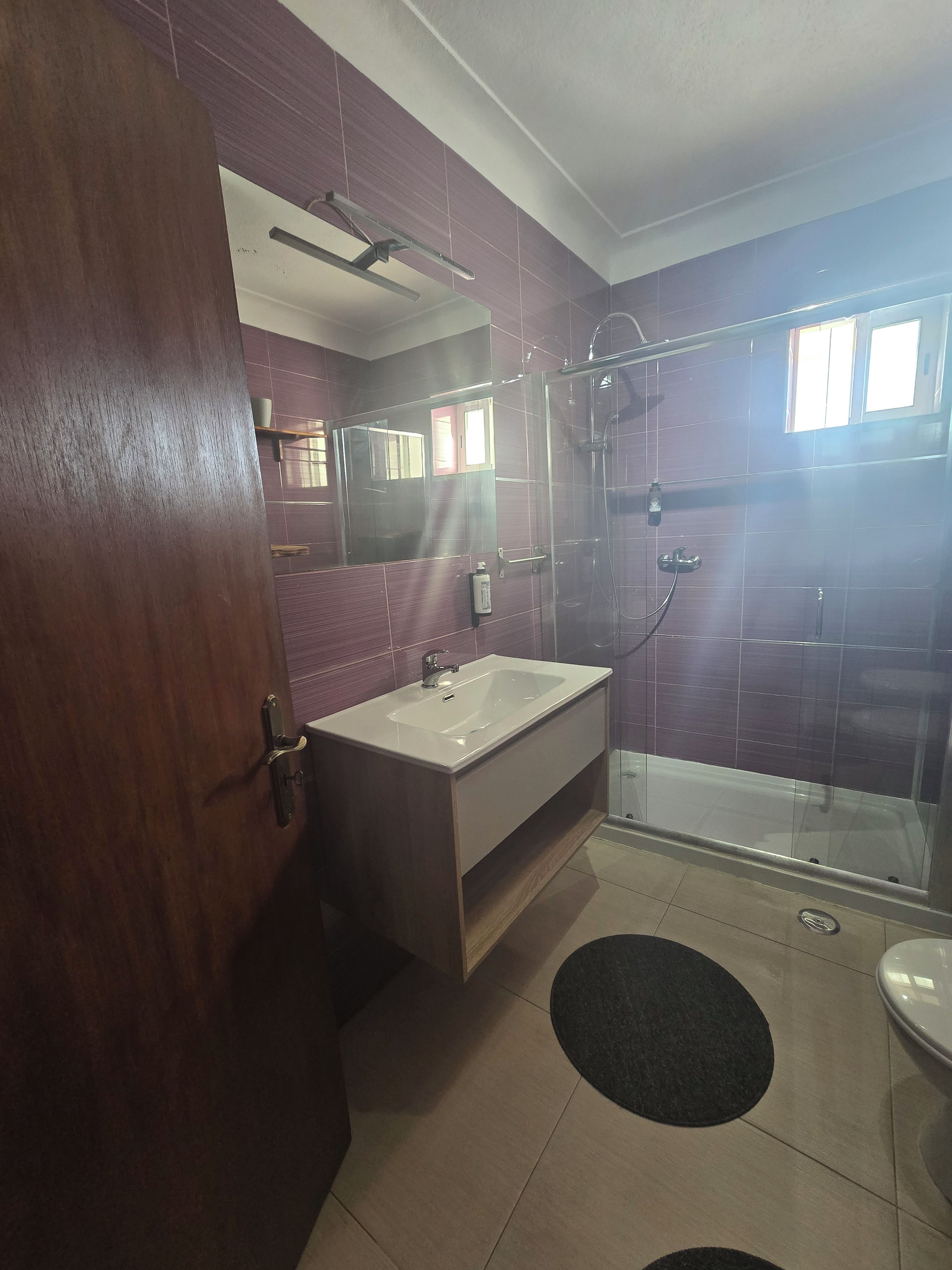 Ein Badezimmer mit Duschkabine aus Glas, einem Waschbecken mit Spiegel darüber und einer Toilette.