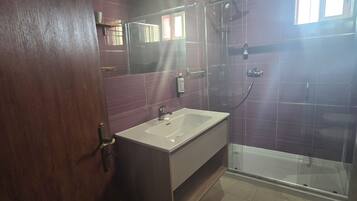 Ein Badezimmer mit Duschkabine aus Glas, einem Waschbecken mit Spiegel darüber und einer Toilette.