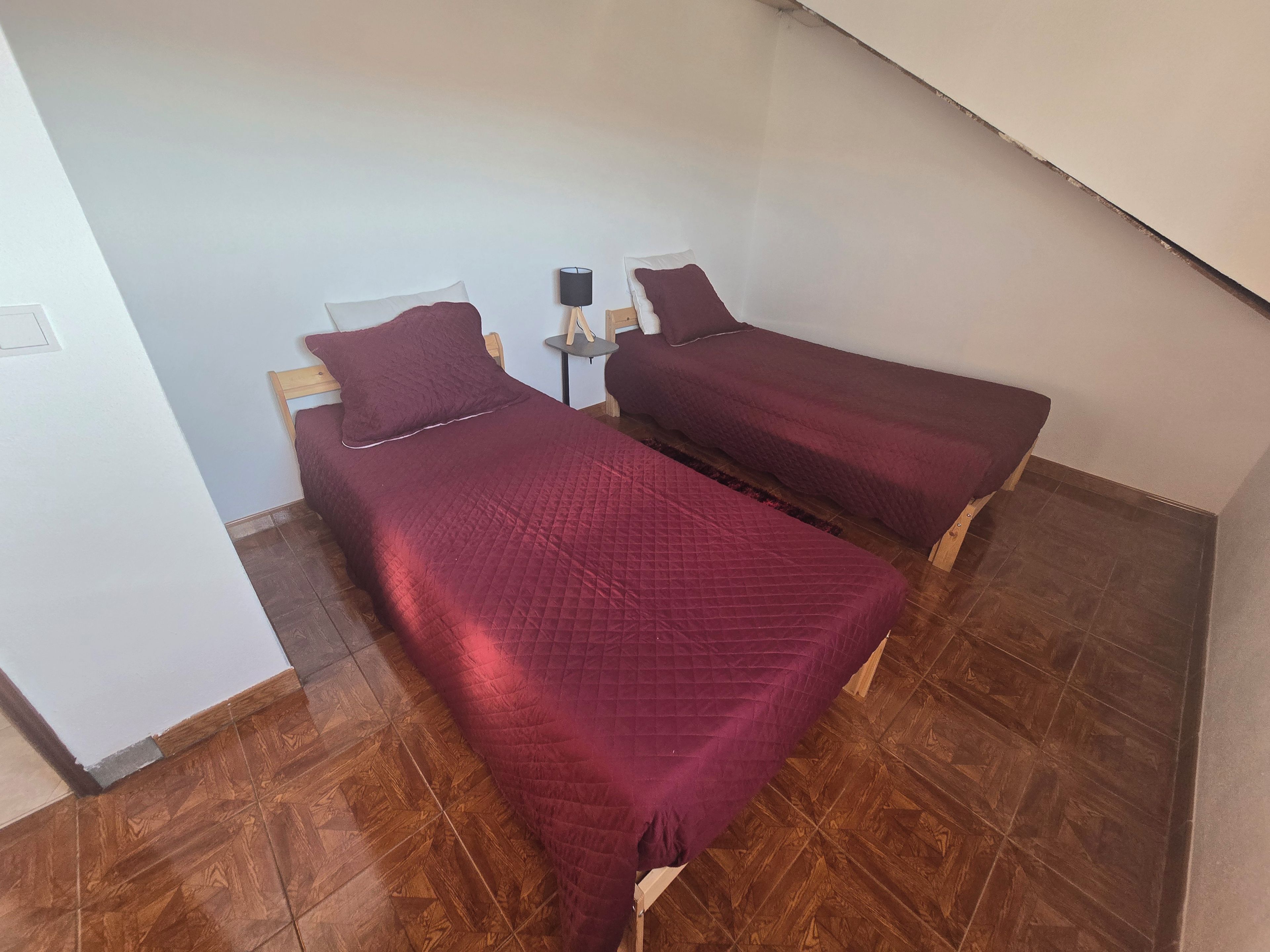 A small room with two beds, a nightstand, and a lamp.