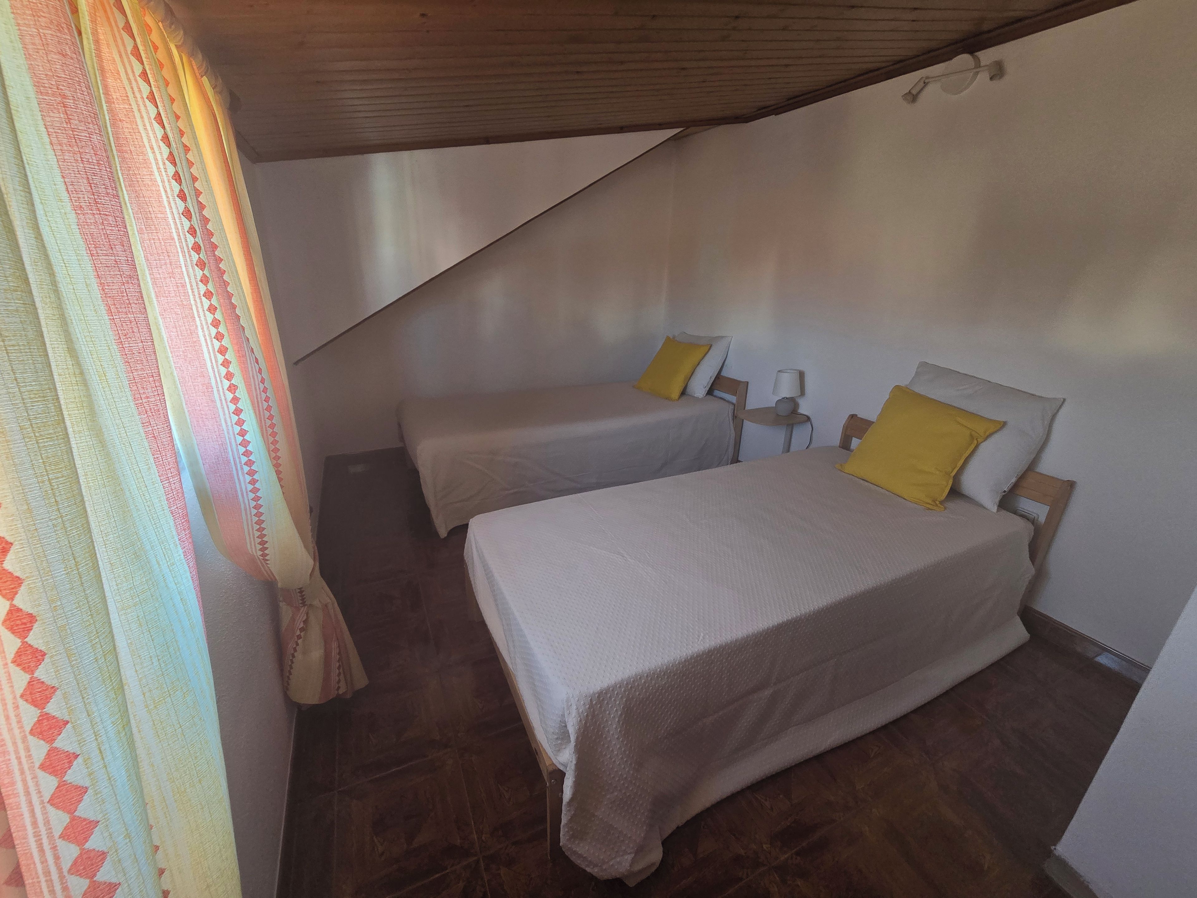 Une chambre avec deux lits, une petite table et un rideau.