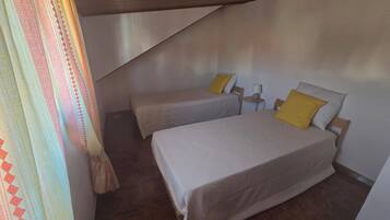 Une chambre avec deux lits, une petite table et un rideau.