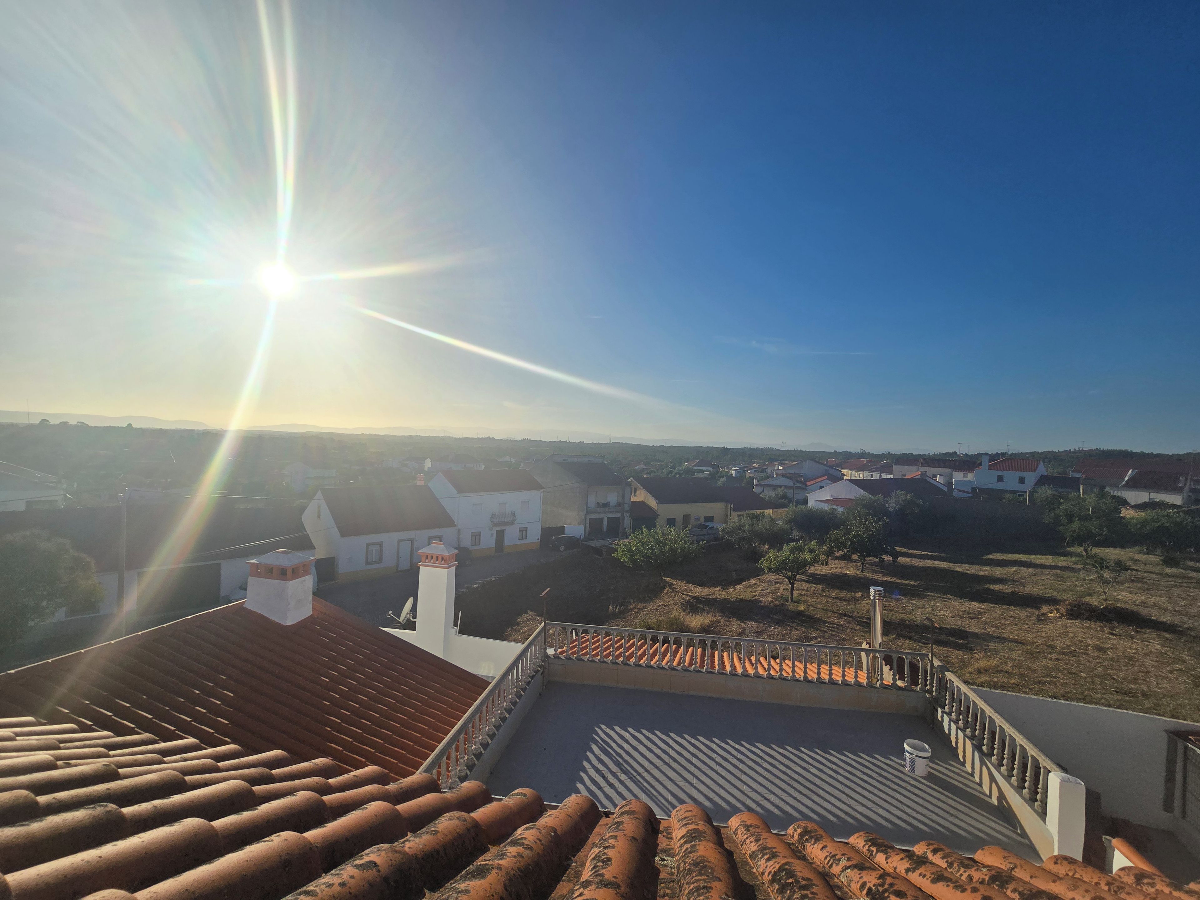 A rooftop terrace with a view of a residential area, including houses and trees.