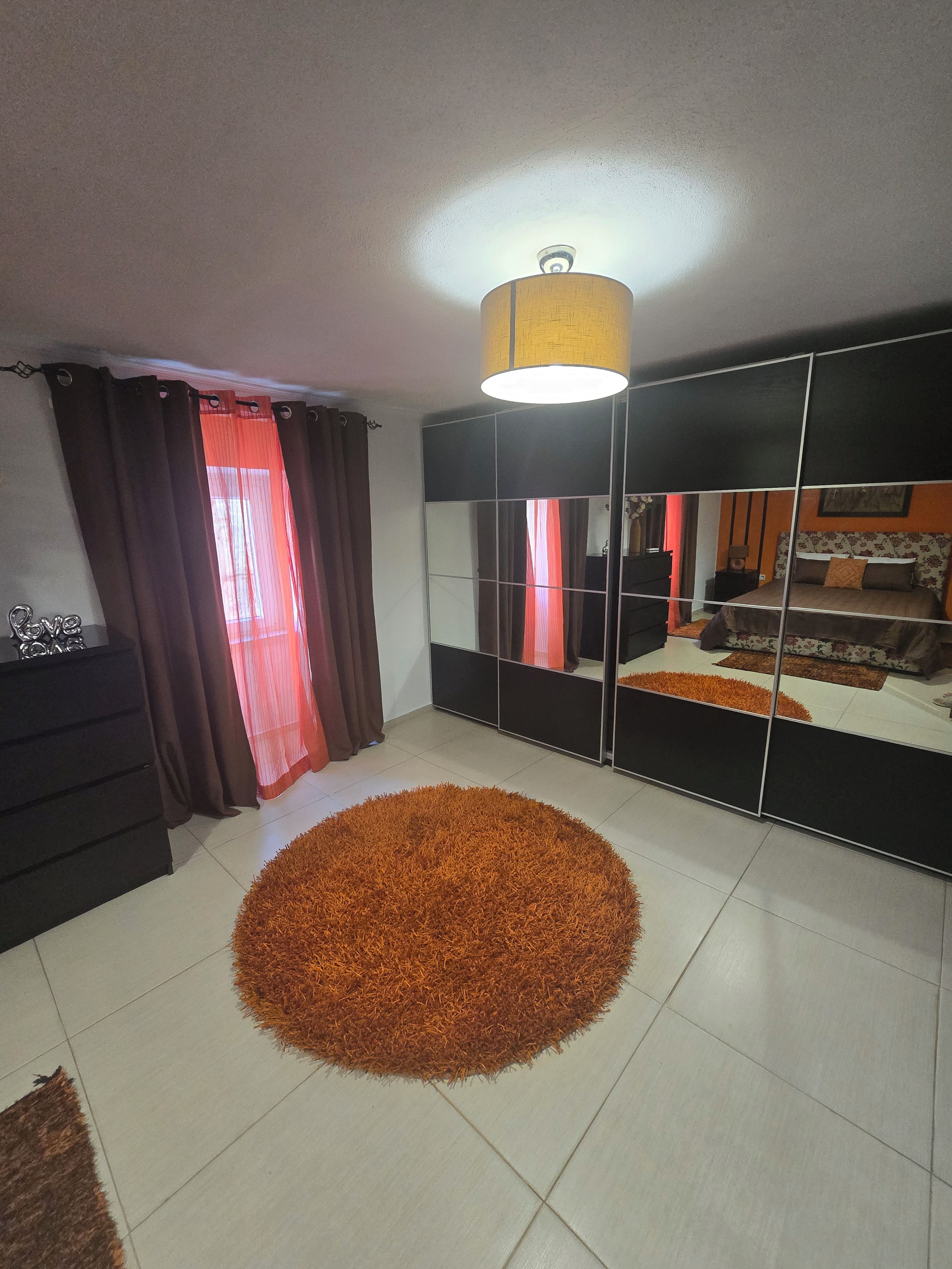 Un dormitorio con cama, espejo, alfombra y cómoda.