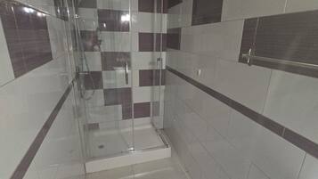 A bathroom with a glass-enclosed shower, tiled walls, and a white sink.