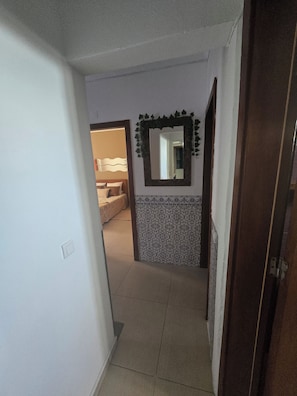 A hallway with a tiled floor, a mirror with a decorative frame, and a patterned wall.