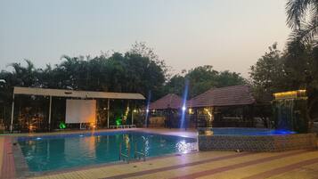 A swimming pool with a tiled deck, a covered seating area, and a water feature.
