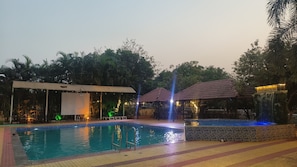 A swimming pool with a tiled deck, a covered seating area, and a water feature.