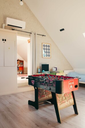 Quarto com mesa de futebol, cama, escrivaninha com computador e janela.