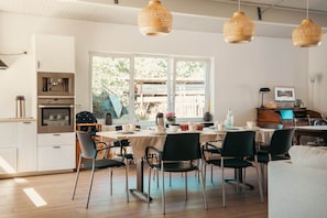 Cozinha moderna com armários brancos, eletrodomésticos de aço inoxidável e um espaço de jantar com mesa posta para quatro pessoas.
