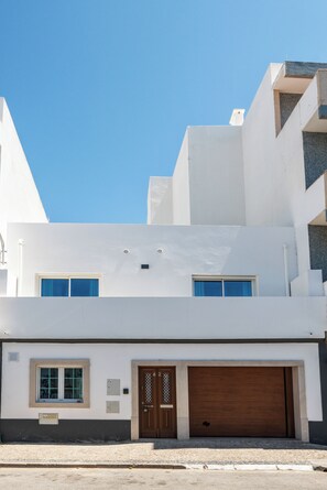 A modern two-story building with a flat roof, a garage door, and a small window with a blue curtain. - Privilege 3-Bedroom Casa dos Capuchinhos in the heart of Faro (Faro)