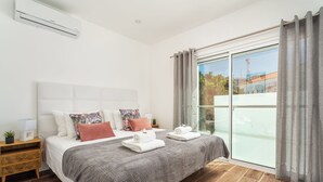 Ein modernes Schlafzimmer mit einem großen Bett, einem Nachttisch, einem Fenster mit Vorhängen und Blick ins Freie.