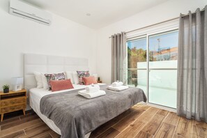 A modern bedroom with a large bed, a nightstand, a window with curtains, and a view of the outside. - Privilege 3-Bedroom Casa dos Capuchinhos in the heart of Faro (Faro)