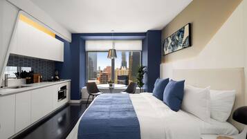 A modern hotel room with a large bed, a dining area, and a view of the cityscape.
